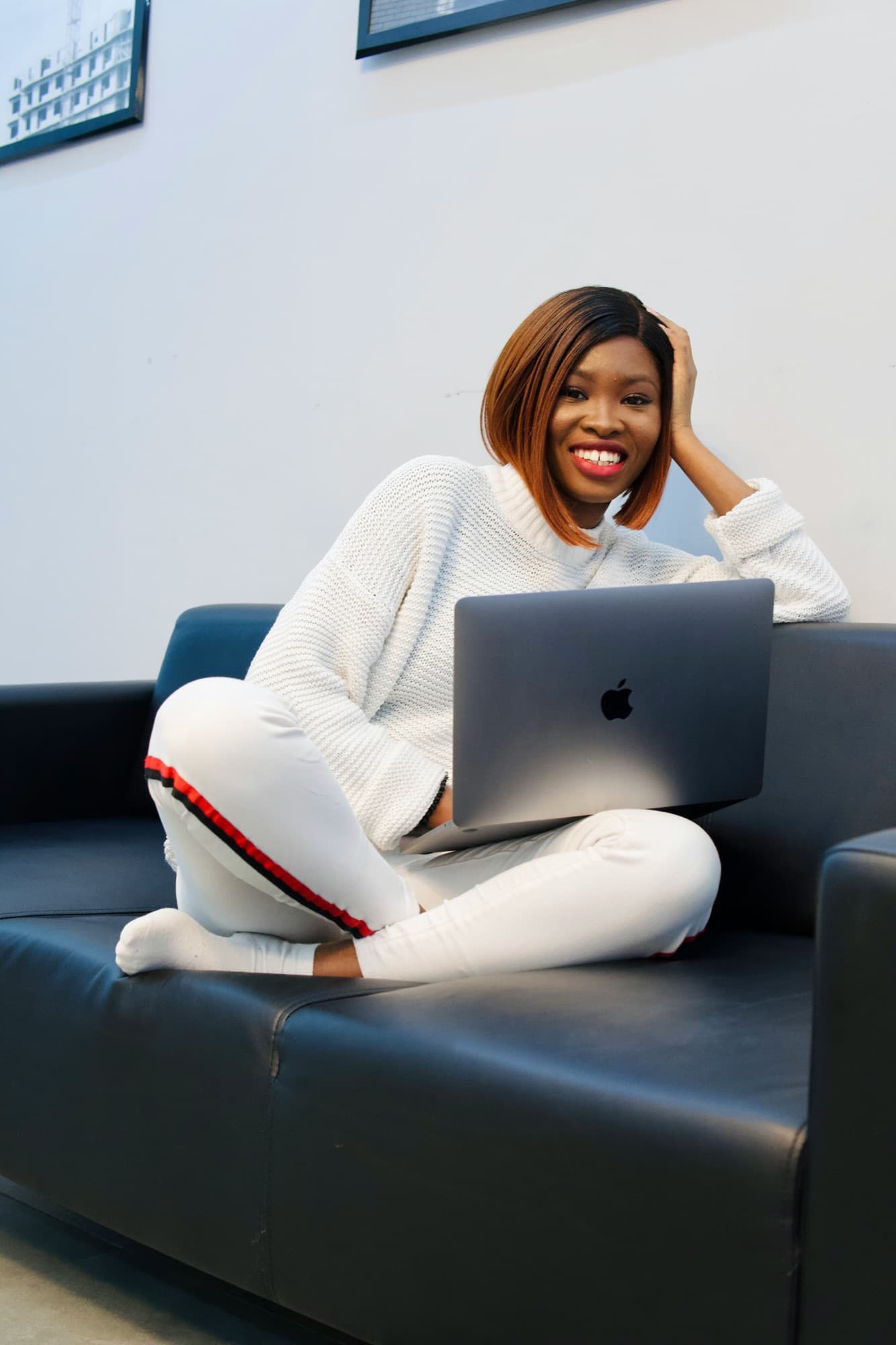 A smiling woman relaxing on a sofa with her laptop in a bright, modern room